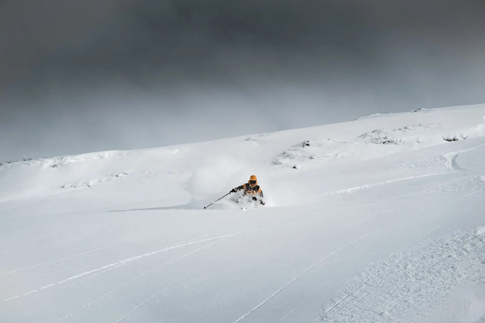 A skier descends an open powder slope beneath dark mountain clouds.